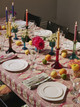 table set with hot pink and multicoloured Mikado inspired embroidered tablecloth and napkins, decorated with oranges and lit candles, evoking a playful, vibrant atmosphere ready for guests